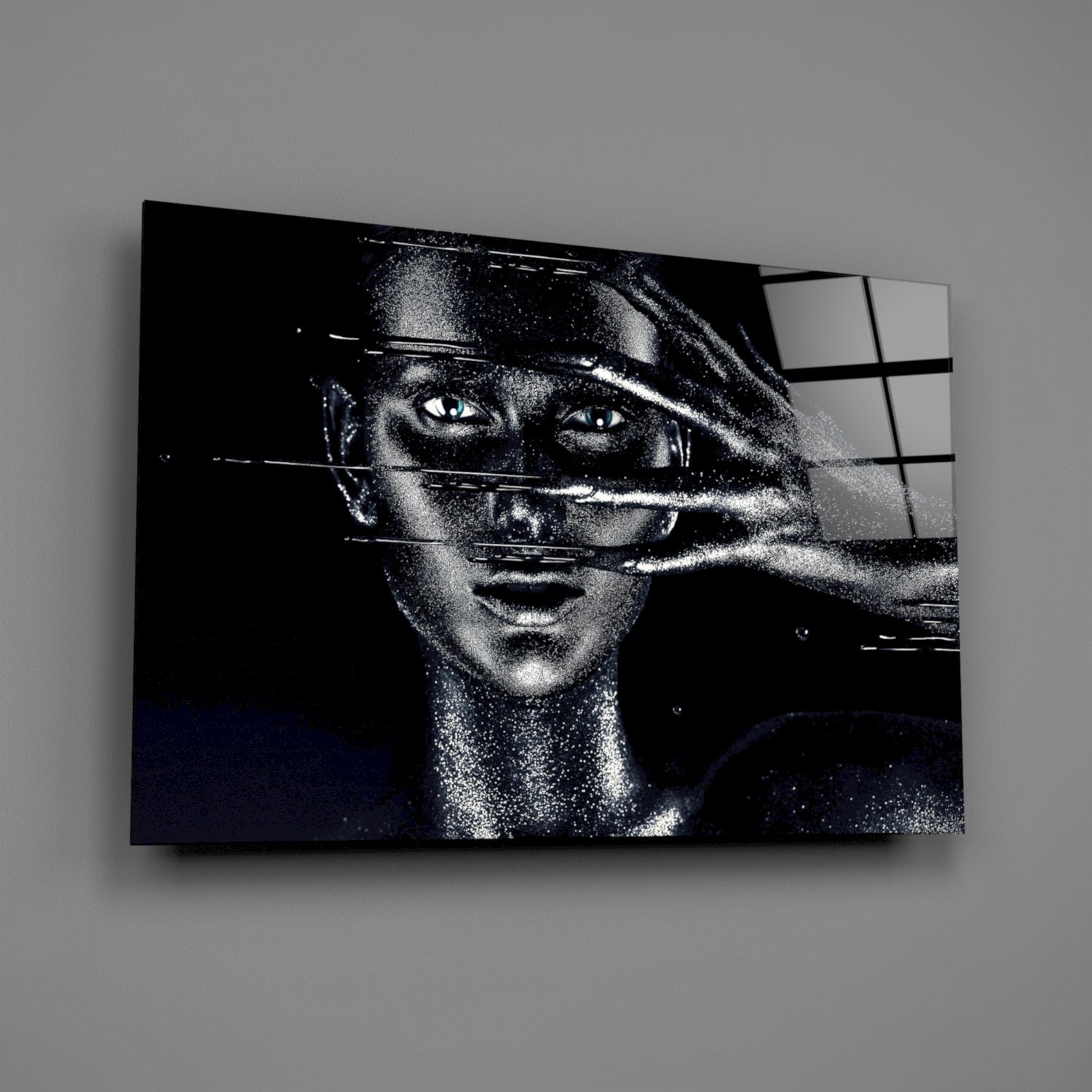 Black and white portrait of a woman with striking eyes on glass panel, displayed at angle against gray wall.