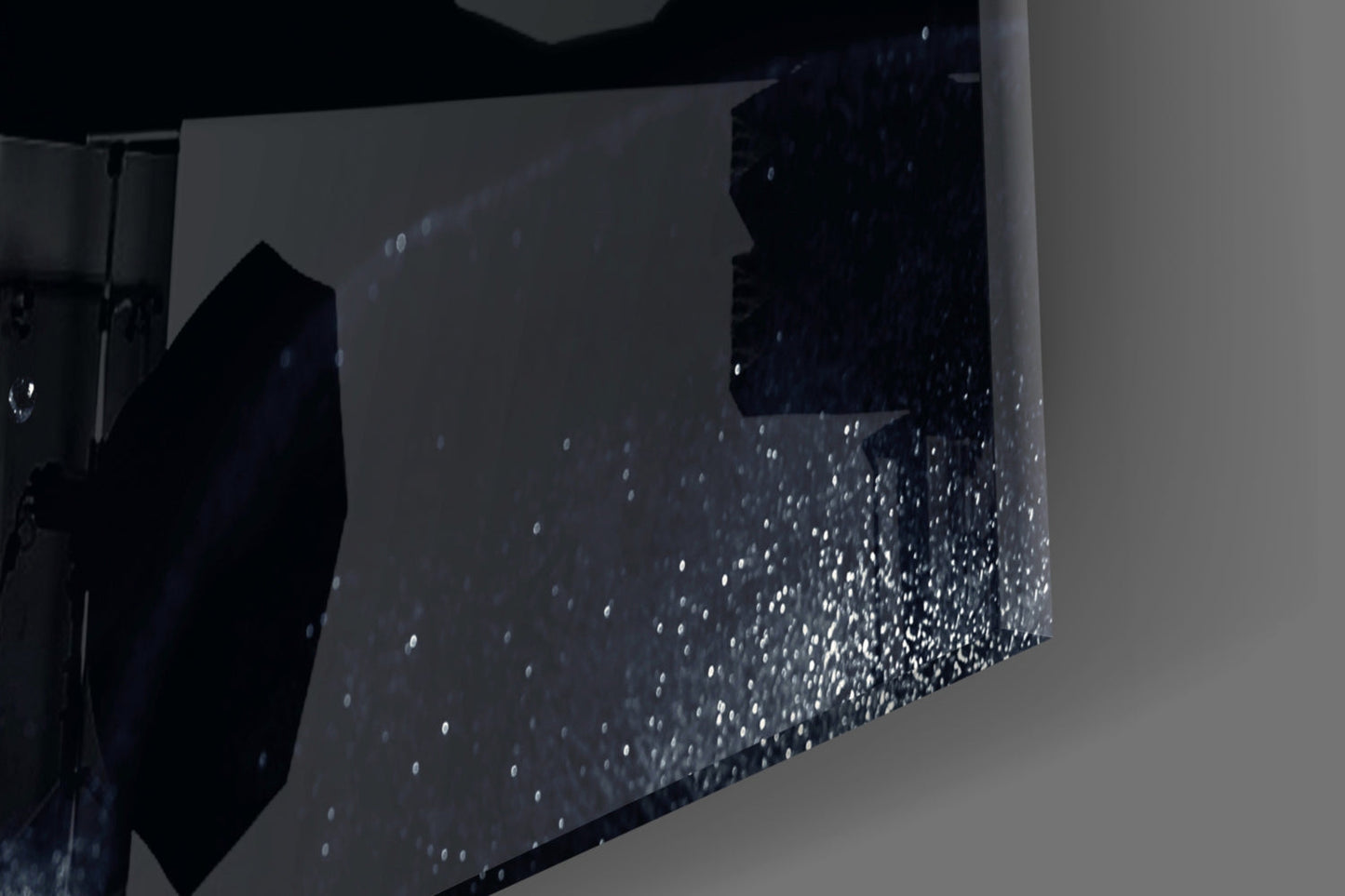 Close-up angle of textured glass wall art showing speckled white particles embedded in dark surface with light gray background.