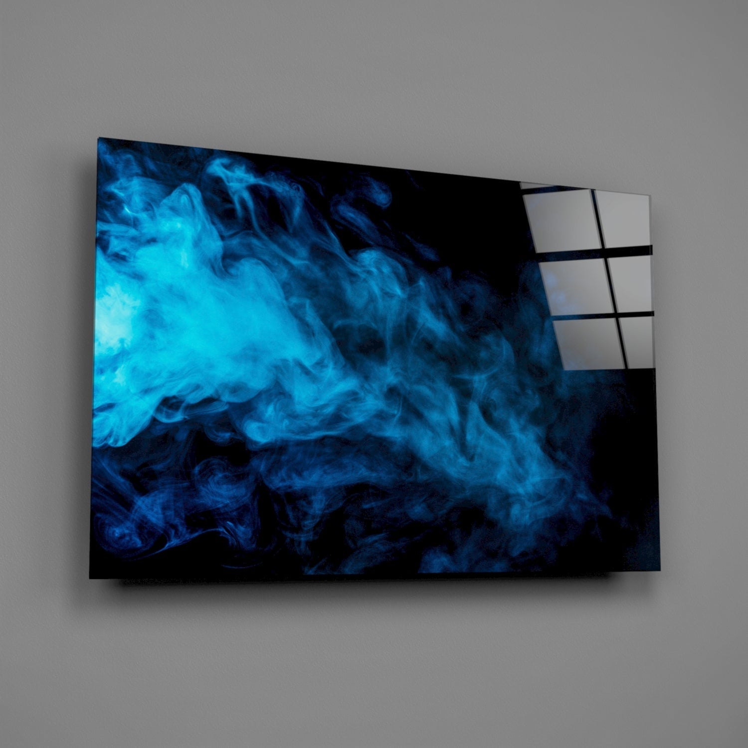 Angled view of blue smoke glass wall art mounted on gray wall, displaying swirling cyan and dark blue smoke patterns with white grid panel visible on right edge.