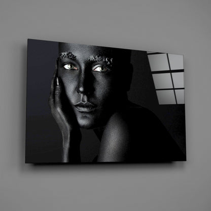 Black and white portrait of a woman with striking eyes on glass wall art, displayed at an angle against a gray wall.