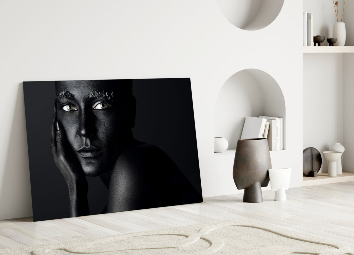 Black and white portrait glass artwork leaning against white wall in minimalist interior with sand and decorative objects.