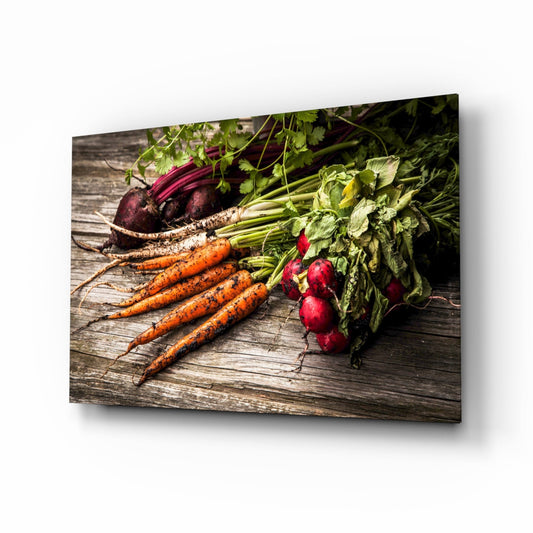 Fresh carrots and radishes with green leafy tops arranged on weathered wood surface, displayed as angled glass wall art.