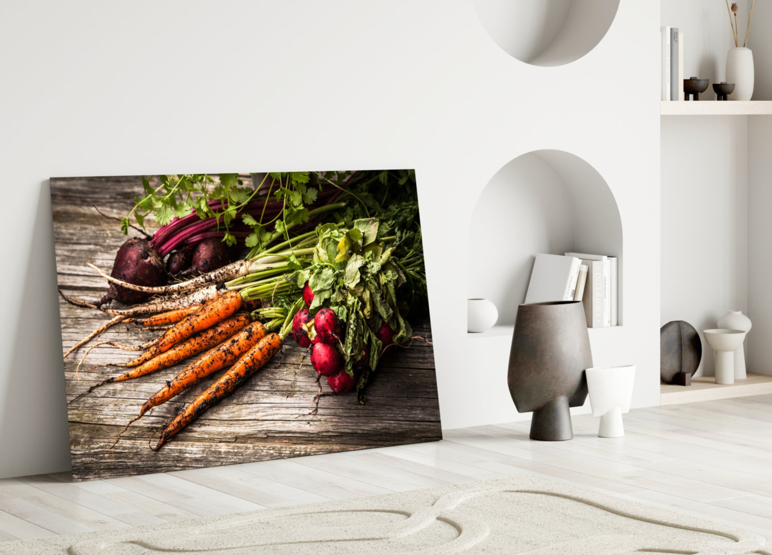 Glass wall art leaning against white wall displays fresh carrots, beets, and radishes on wooden surface.