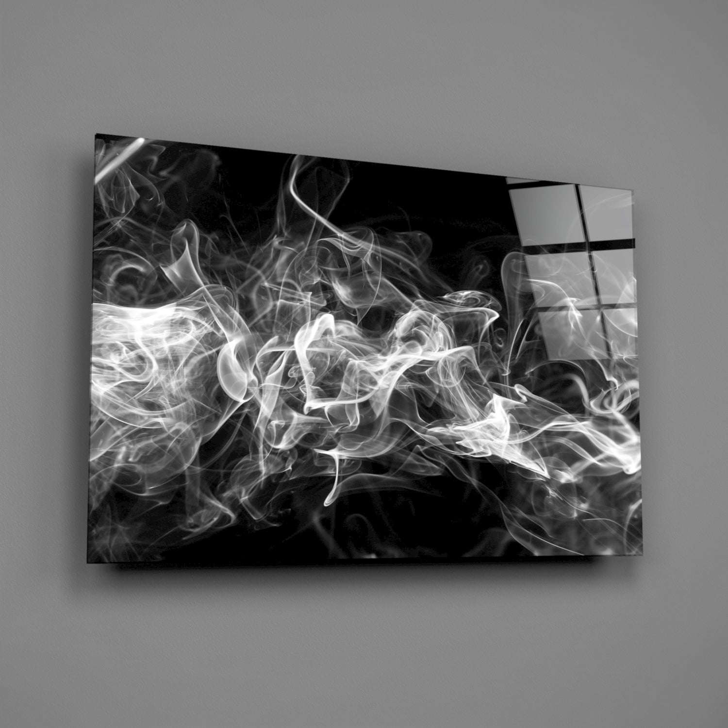 Black and white glass wall art panel displaying swirling smoke patterns mounted on gray wall at angle.
