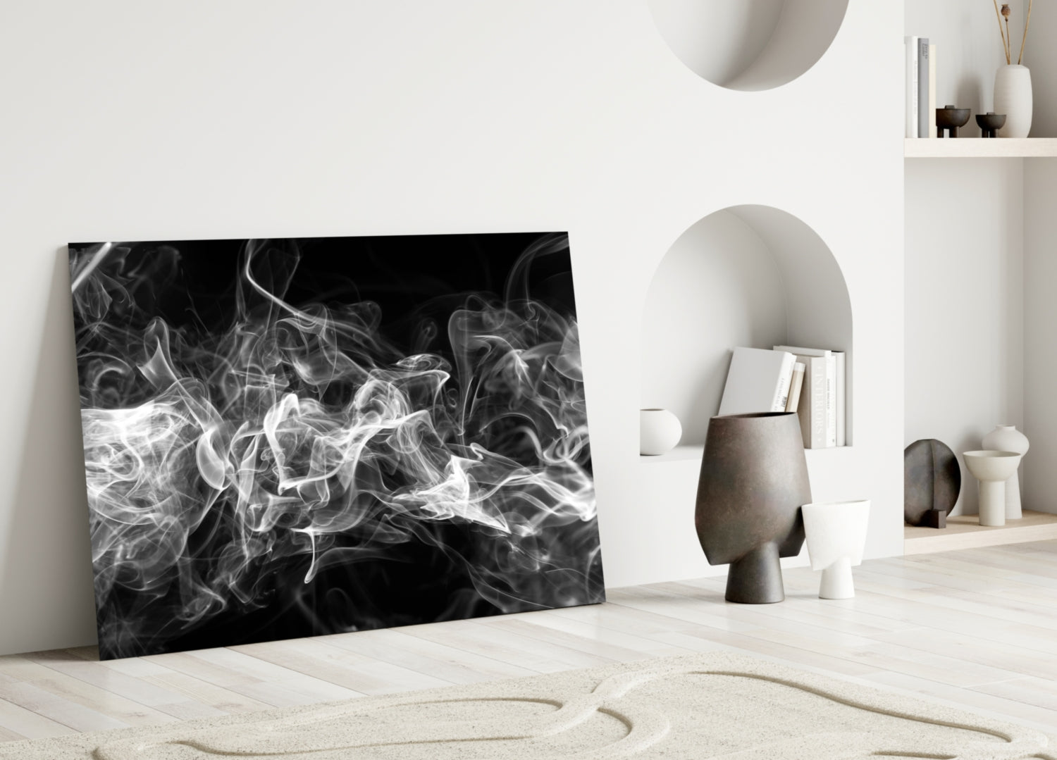 Black and white swirling smoke glass artwork leaning against white wall in minimalist room setting with ceramic vessels.