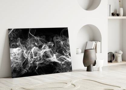 Black and white swirling smoke glass artwork leaning against white wall in minimalist room setting with ceramic vessels.