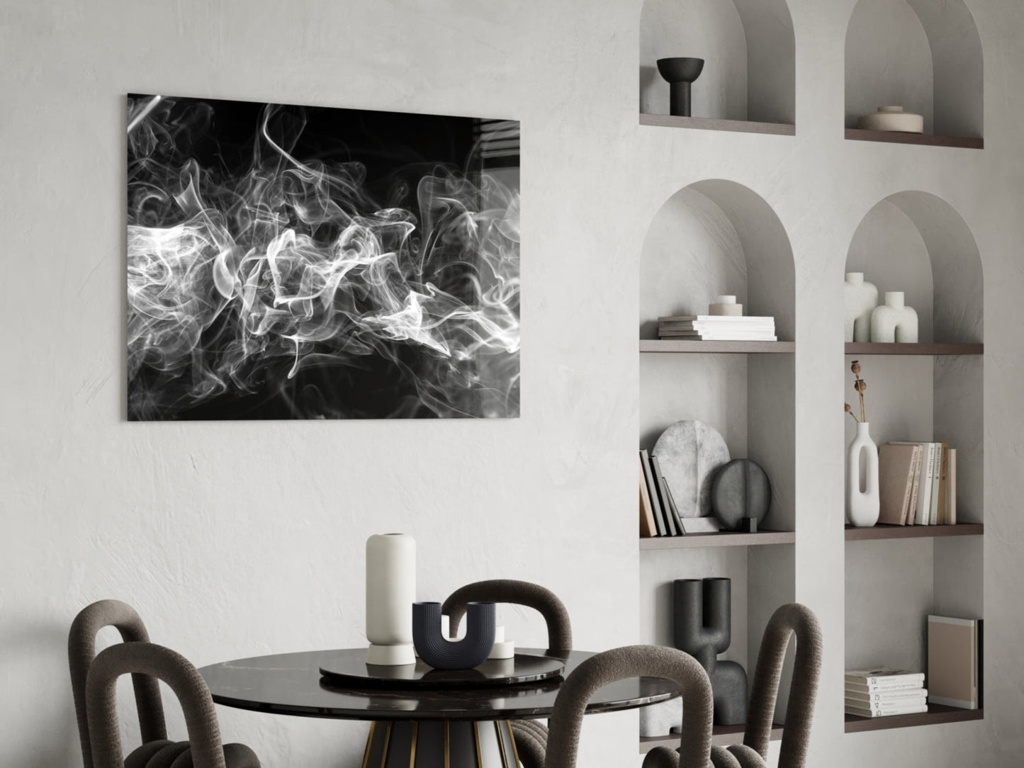 Black and white abstract smoke swirl glass artwork displayed above round black dining table with curved beige chairs and white shelving unit.