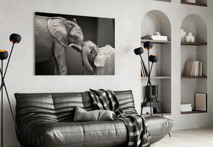 Black and white glass wall art of adult elephant with baby elephant displayed above gray leather sofa in modern living room interior.