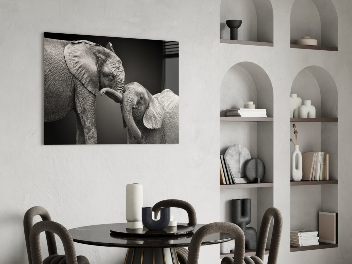 Black and white glass wall art depicting an adult elephant with its trunk touching a young elephant calf, displayed above a dining table.