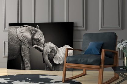 Black and white glass wall art depicting adult elephant with baby elephant against dark background, displayed in modern living room setting.