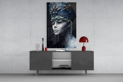 Glass wall art featuring a monochromatic female portrait with ornate blue headdress and beaded details displayed above a modern gray console table.
