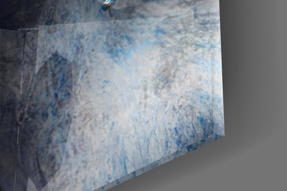 Close-up angled view of glass wall art showing blue and white textured brushstroke details on transparent material.