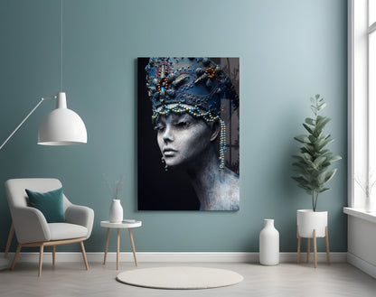 Glass wall art depicting a gray-skinned woman's profile with ornate blue headdress and beaded jewelry against dark background, displayed in modern room setting.