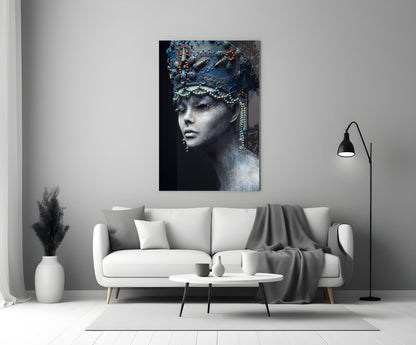 Glass wall art depicting a woman's profile with ornate blue headdress and gold beaded details against dark background, displayed above white sofa in modern living room.