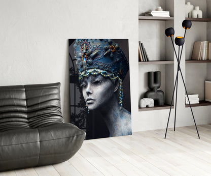 Modern living room interior featuring blue-toned glass wall art of a woman's profile with ornate headpiece displayed between gray sofa and shelving unit.