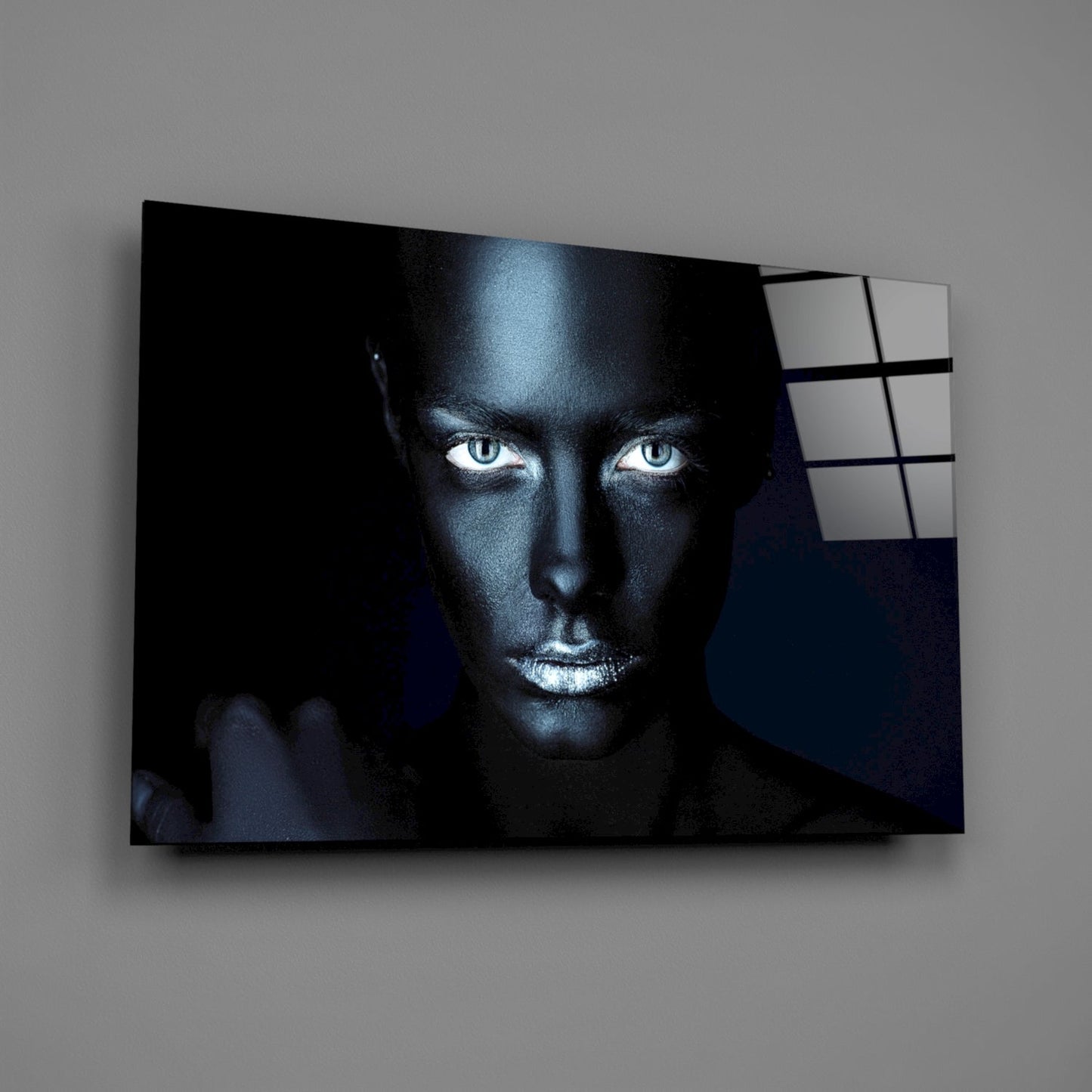 Glass wall art displaying a dramatic portrait of a woman with striking blue eyes against a dark background, mounted on a gray wall.