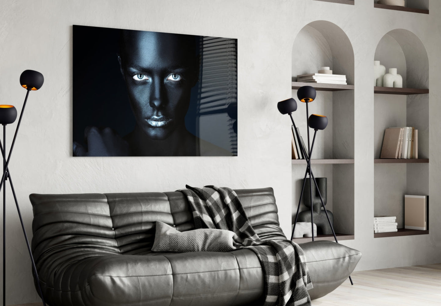 Modern living room with black leather sofa displaying glass wall art of woman's face with glowing blue eyes against dark background.
