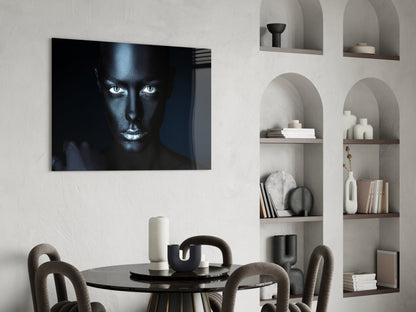 Glass wall art featuring a high-contrast portrait of a woman's face with striking white eyes against black skin tones, displayed above a round dining table.