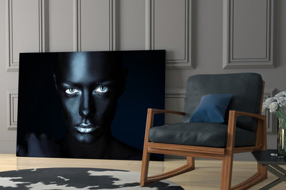 Black glass wall art featuring a woman's face with striking white eyes against dark skin, displayed in a modern living room setting.