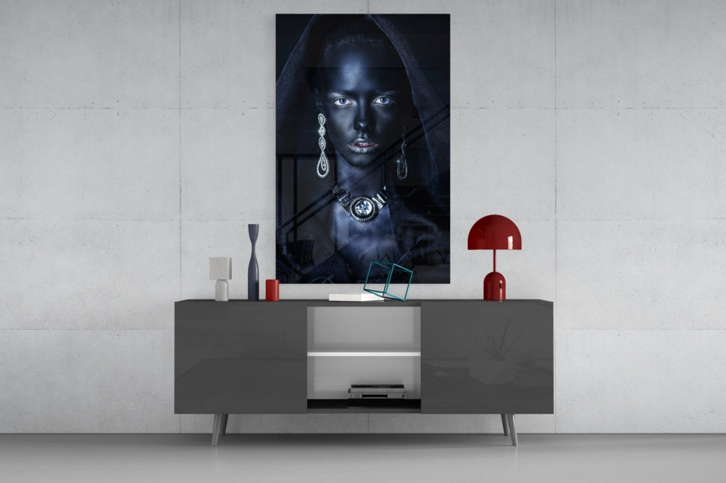 Glass wall art featuring portrait of woman with dark skin, silver jewelry, and black hood displayed above gray console table with red accents.