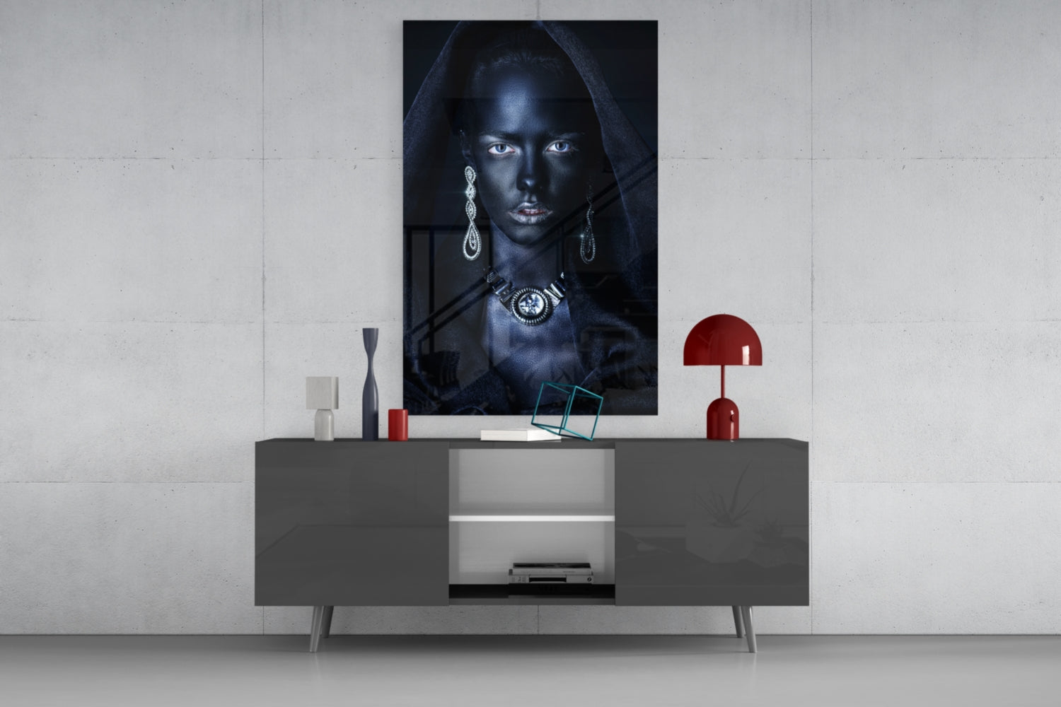 Glass wall art featuring portrait of woman with dark skin, silver jewelry, and black hood displayed above gray console table with red accents.
