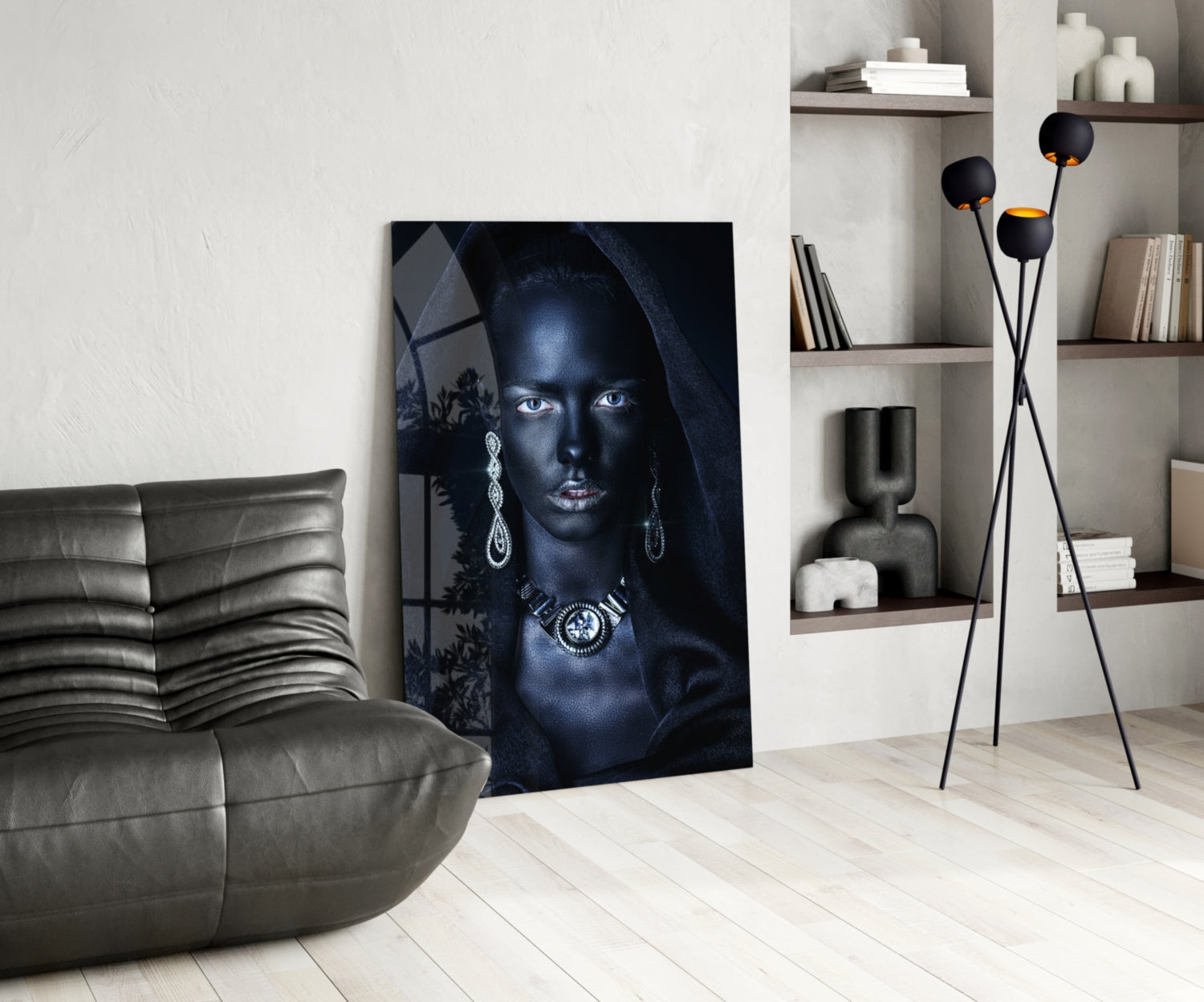 Modern living room interior featuring a glass portrait artwork of a woman with blue eyes and jewelry, displayed next to a gray leather sofa.