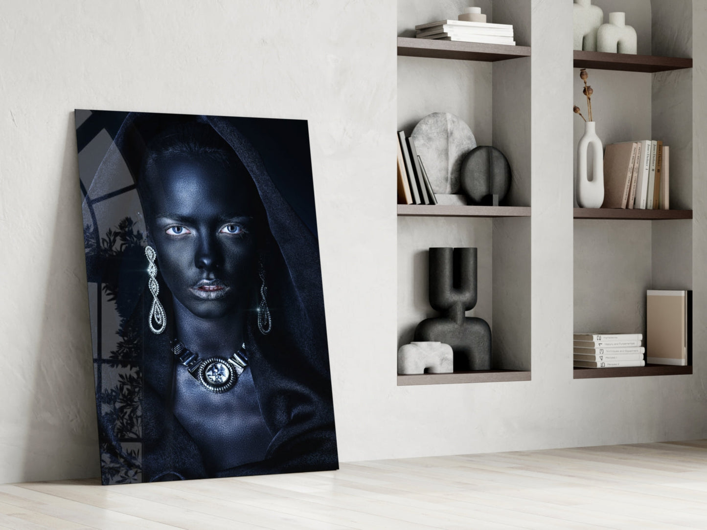 Glass wall art featuring a blue-toned portrait of a woman with striking eyes and ornate jewelry, leaning against white wall beside shelving.