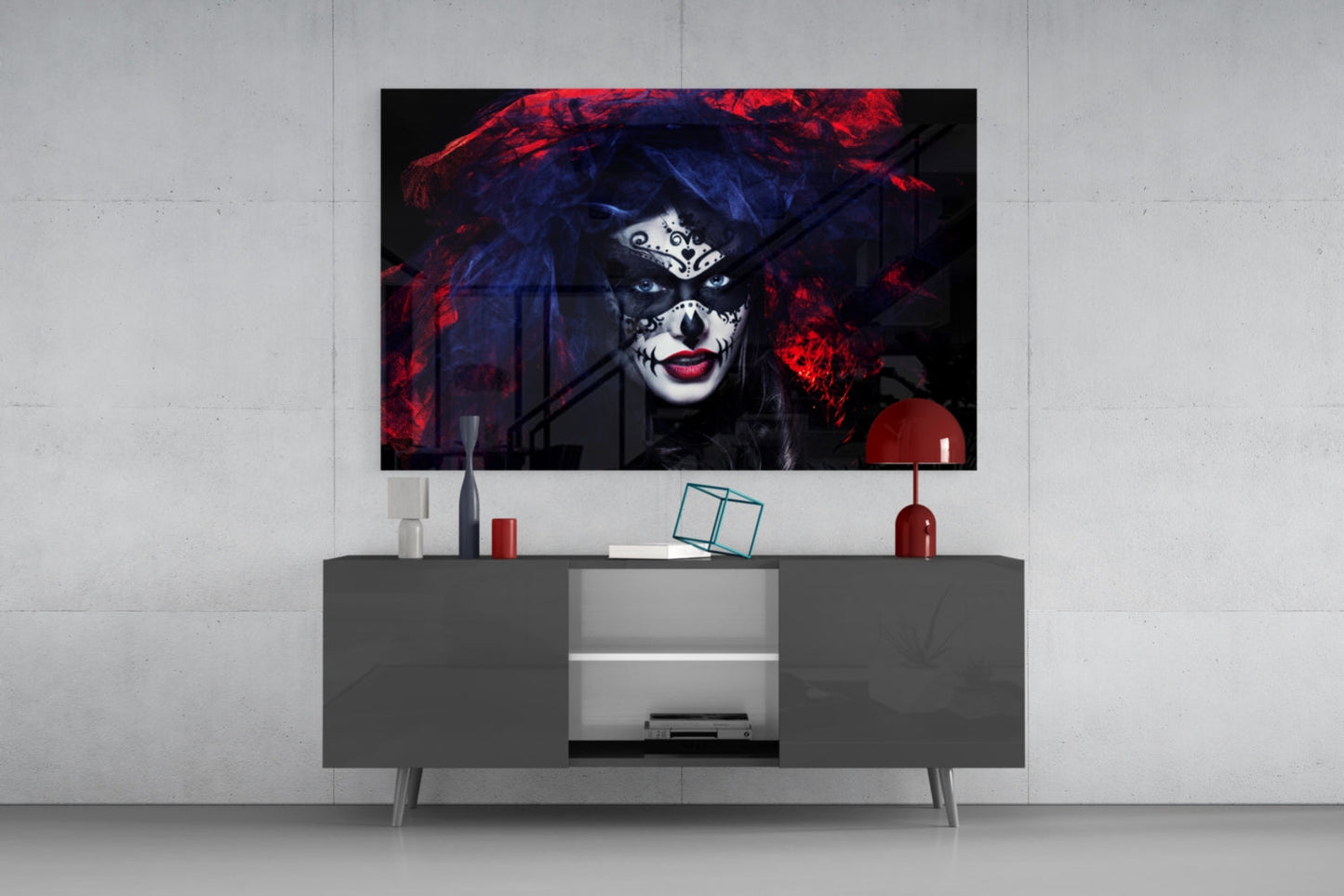 Glass wall art depicting woman with skull face makeup, red and blue lighting, displayed above gray media console in modern living room setting.