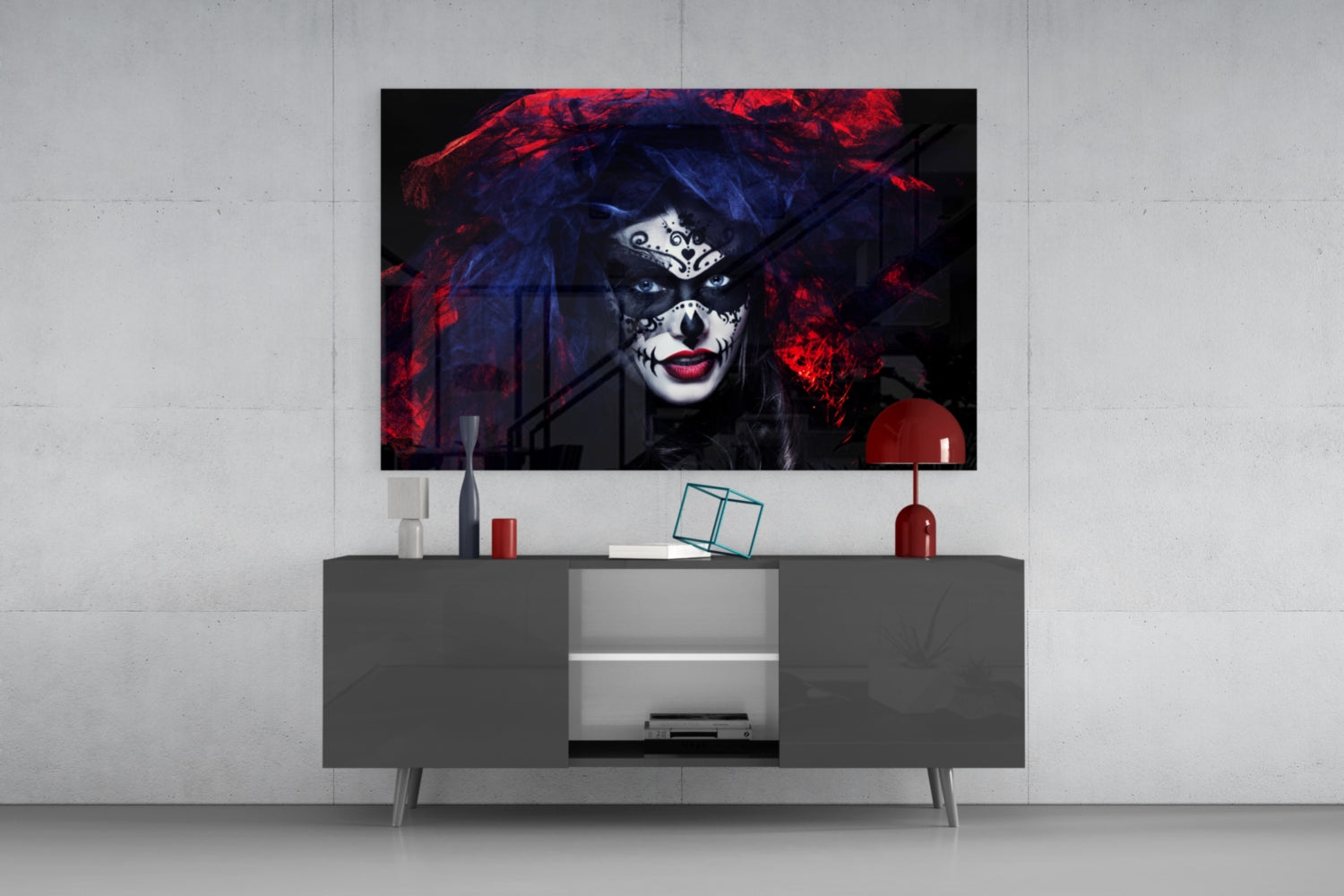 Glass wall art depicting woman with skull face makeup, red and blue lighting, displayed above gray media console in modern living room setting.