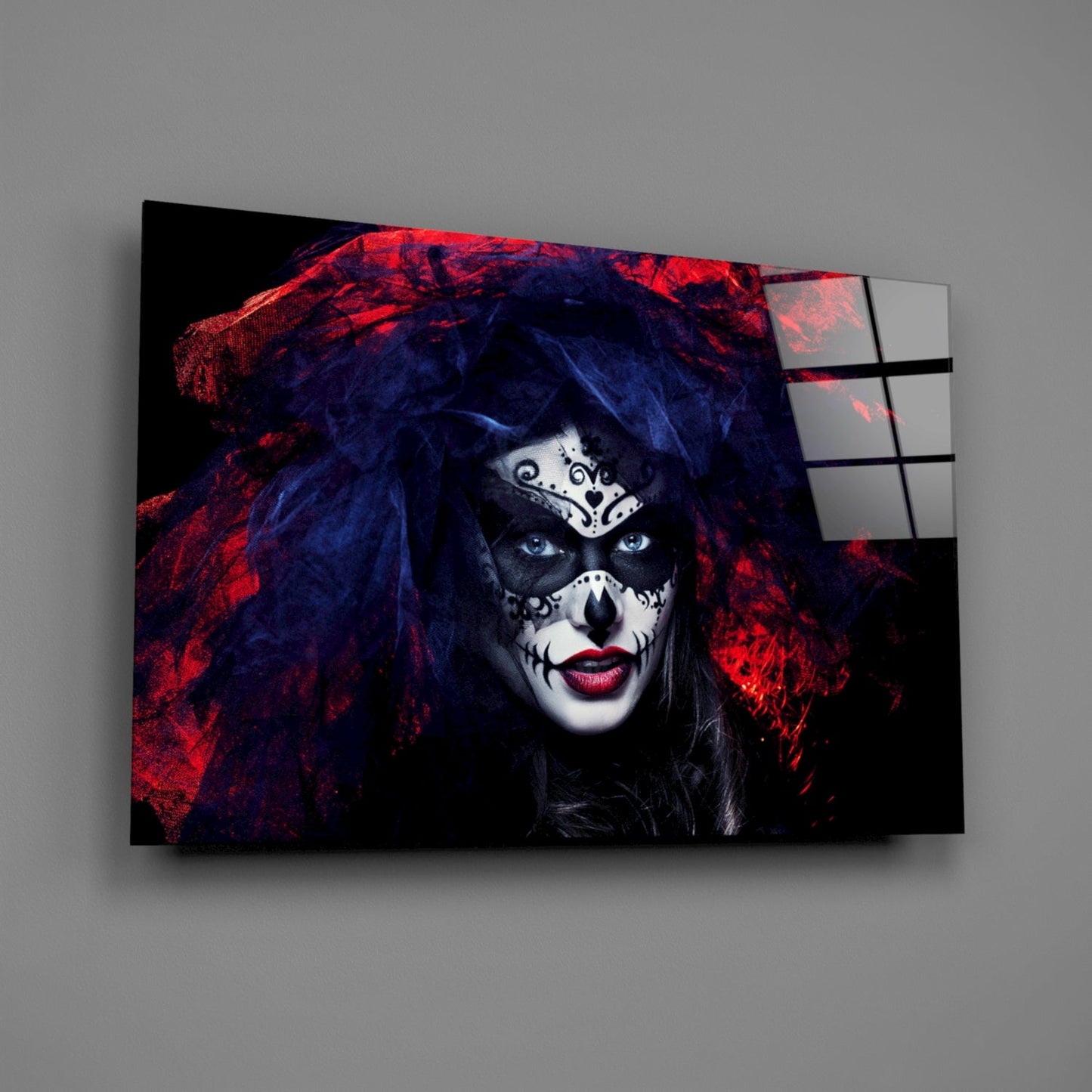 Woman with skull face makeup and blue hair wearing red and black fabric, displayed on glass wall art panel angled against gray background.