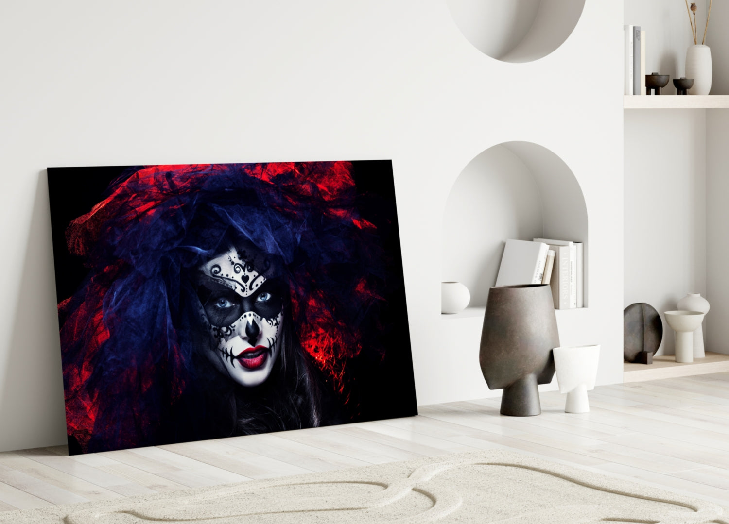 Glass wall art depicting woman with dramatic skull makeup, red hair, and dark blue-black face against black background, displayed leaning against white wall in minimalist room.