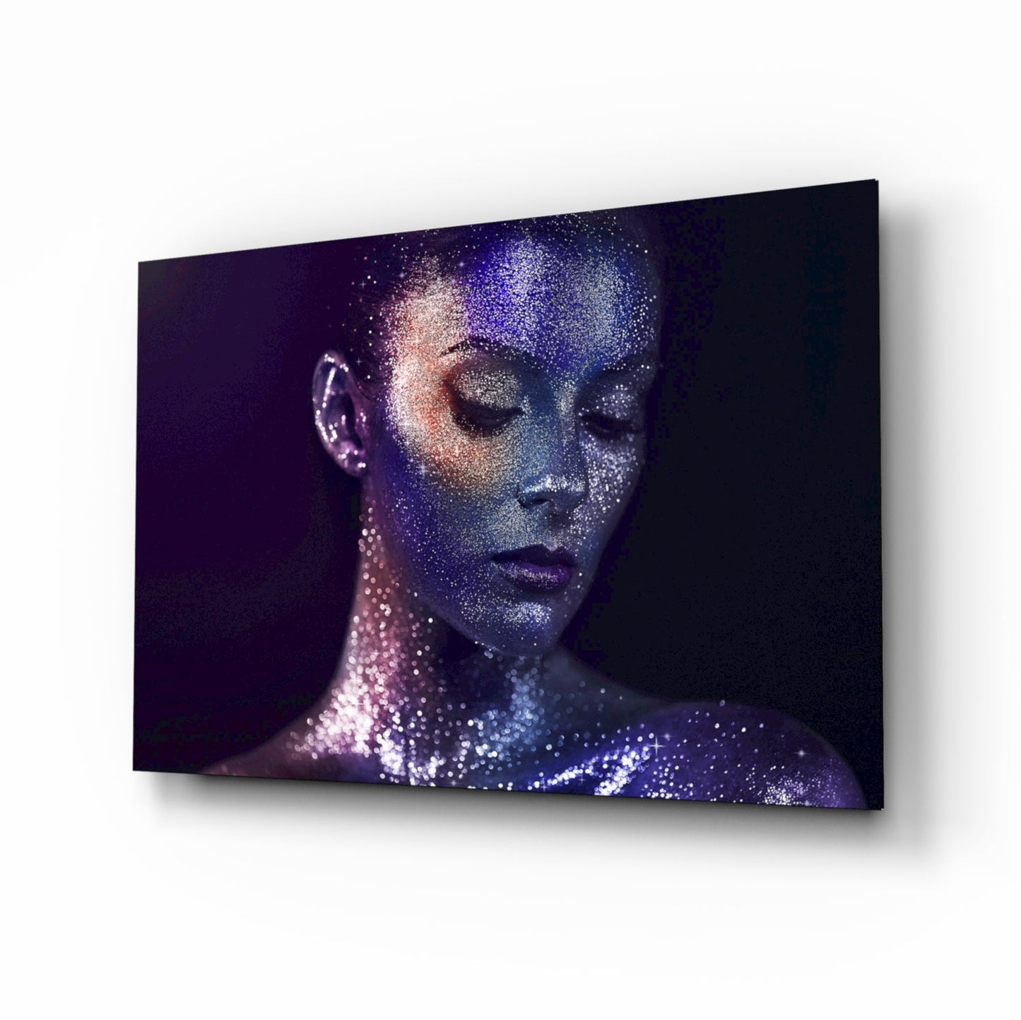 Woman's face in profile with closed eyes covered in blue and pink glittery particles against dark background on glass wall art.