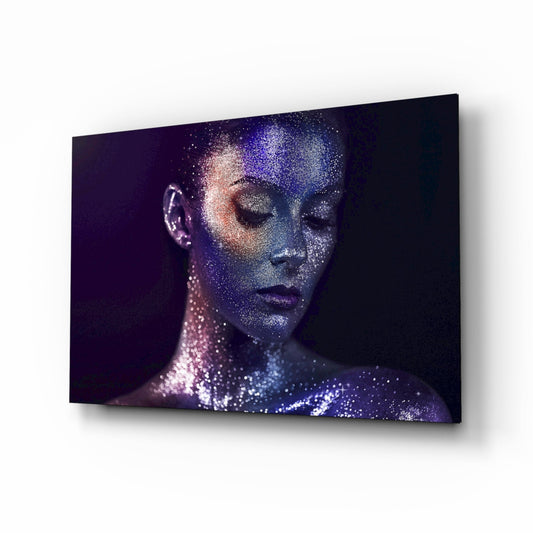 Woman's face in profile with closed eyes covered in blue and pink glittery particles against dark background on glass wall art.
