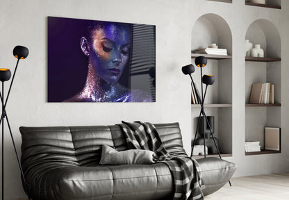 Modern living room with black leather sofa displaying glass wall art of woman's face with blue and purple sparkle effects.