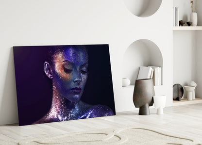 Glass wall art leaning against white wall displays profile of woman's face with purple and blue glitter effect on dark background.