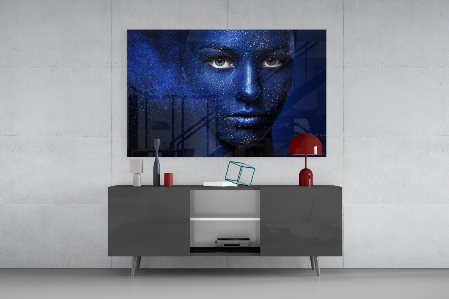 Modern living room display with blue glass wall art featuring a woman's face above a dark gray media console with red decorative accents.