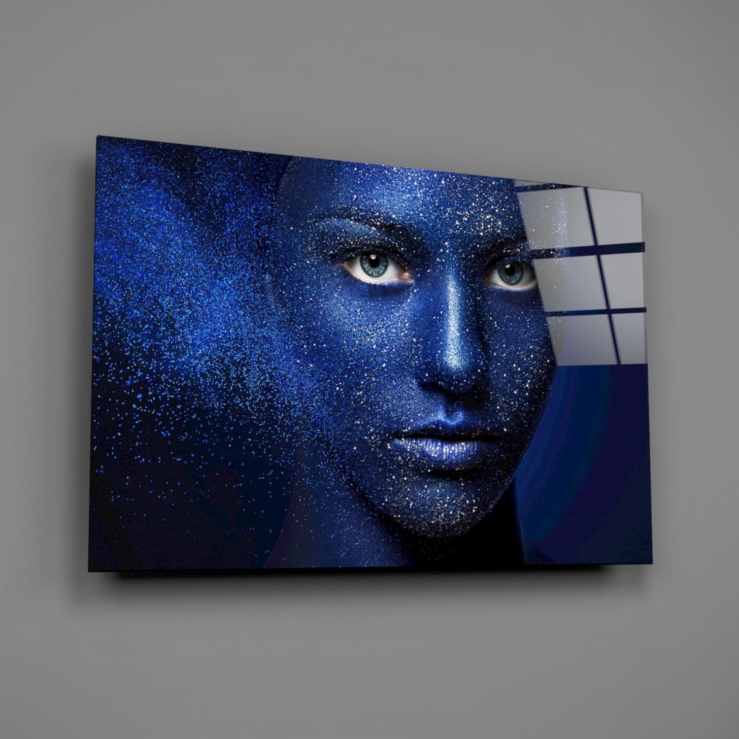 Blue-toned woman's face with glittering effect mounted on wall, partially overlapped by white and navy glass panels.