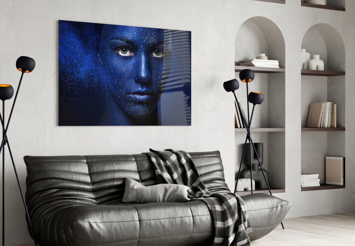 Blue-toned woman's face portrait displayed on glass wall art above black leather sofa in modern living room setting.