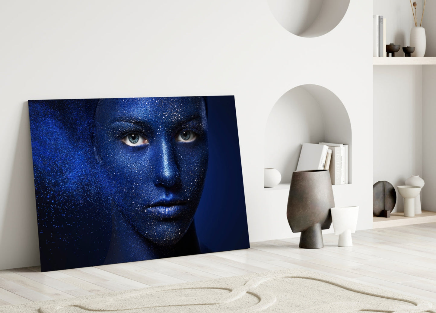 Blue glitter-textured portrait glass artwork leaning against white wall in minimalist interior setting with sculptural decor.