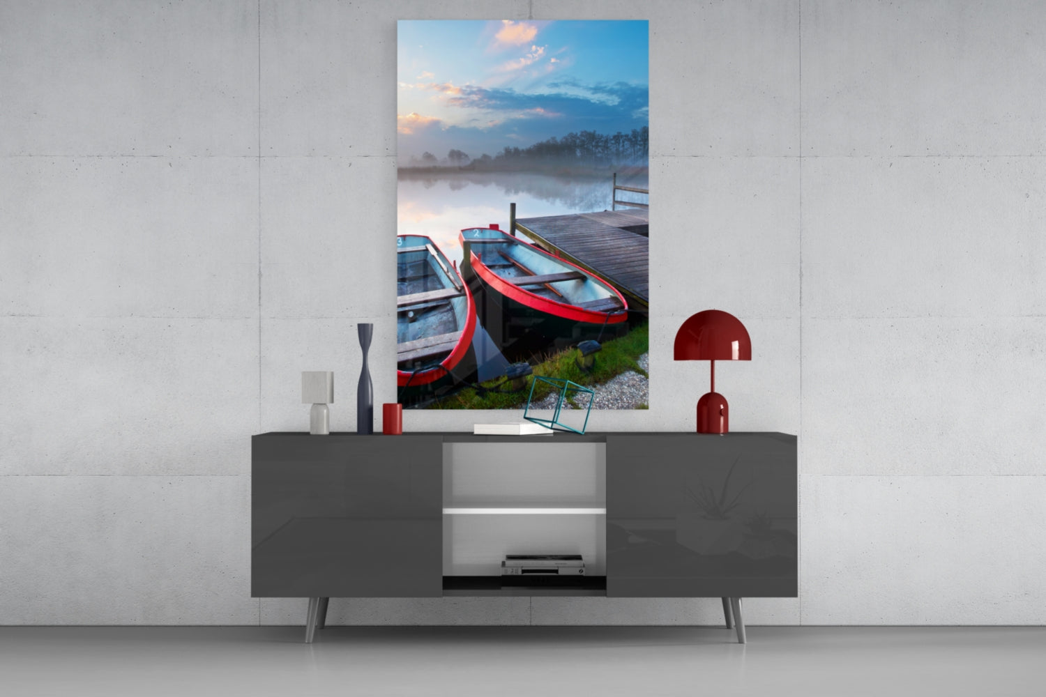 Glass wall art depicting red and blue boats moored at a wooden dock beside a misty lake at sunrise, displayed above a gray media console.