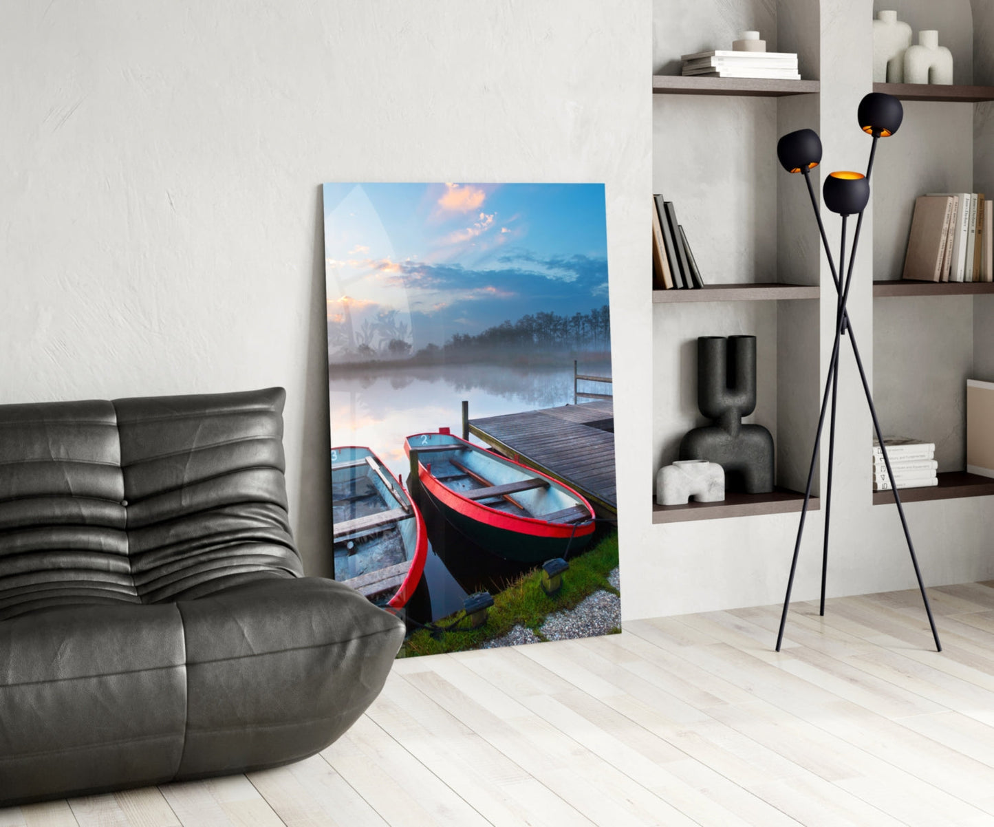 Glass wall art depicting red boats on a misty lake at sunrise displayed in a modern living room beside a gray leather chair.