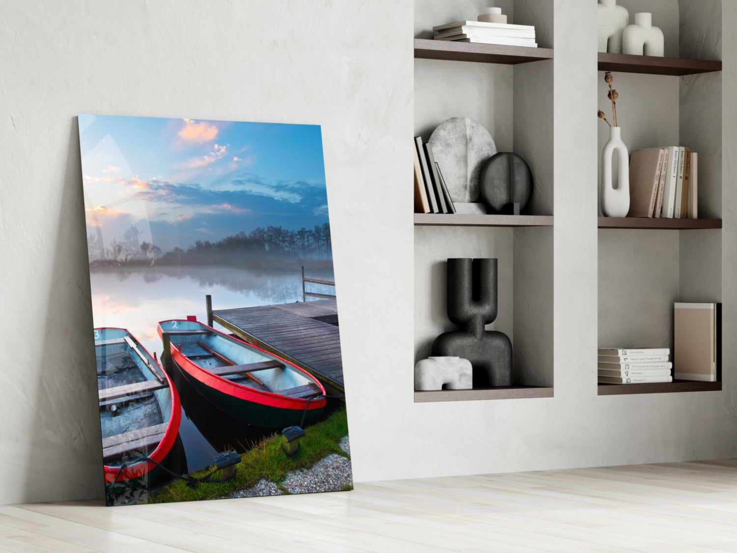 Glass wall art leaning against white wall displays red and blue boats on misty lake at dawn, styled with home décor shelving.