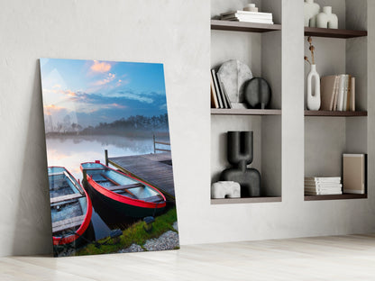 Glass wall art leaning against white wall displays red and blue boats on misty lake at dawn, styled with home décor shelving.