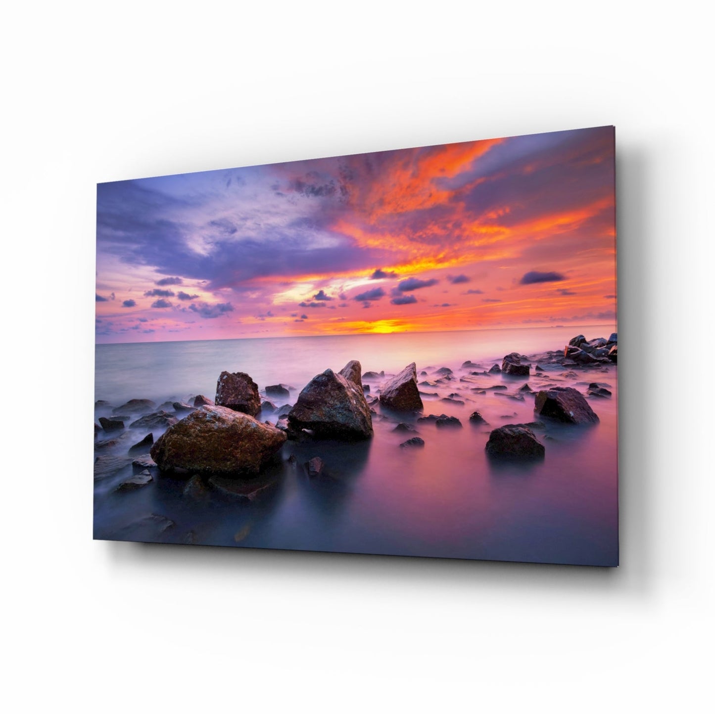 Canvas wall art displaying a rocky coastline at sunset with vibrant orange and purple sky reflecting on calm pink water.