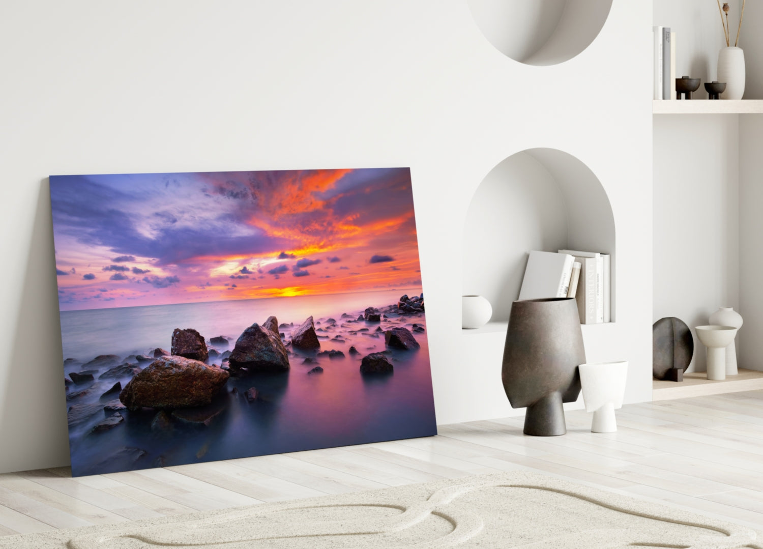 Framed sunset seascape canvas leaning against white wall in minimalist interior with decorative objects.