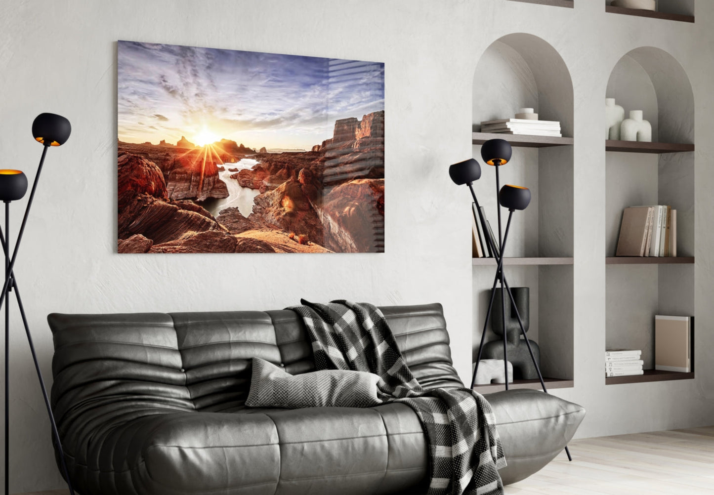 Canyon and Sunset glass wall art displaying a golden sunrise over red rock formations and water, displayed above a black leather sofa in a modern living room.