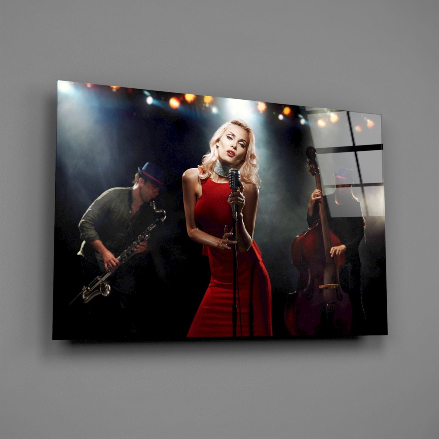 Glass wall art mounted on gray wall displaying female vocalist in red dress with saxophonist and cellist performing on stage with stage lights.