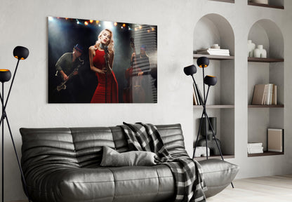 Glass wall art depicting female singer in red dress with saxophonist on stage, displayed above black leather sofa in modern living room.