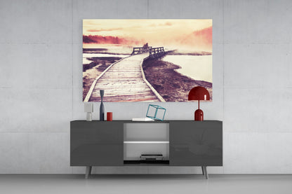 Glass wall art depicting a wooden boardwalk extending into misty water at sunset, displayed above a dark media console.