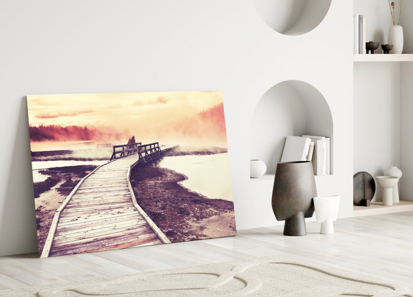 Canvas print leaning against white wall showing wooden boardwalk extending toward misty lake and forest at sunset.